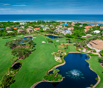 Aerial view of Hideaway Beach Club golf course with lakes, greenery, and Gulf of Mexico coastline.