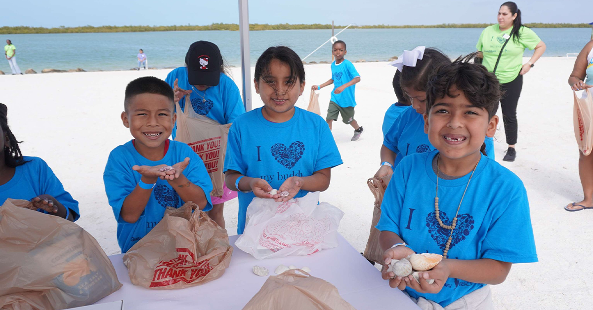 Children in blue shirts holding seashells at beach table