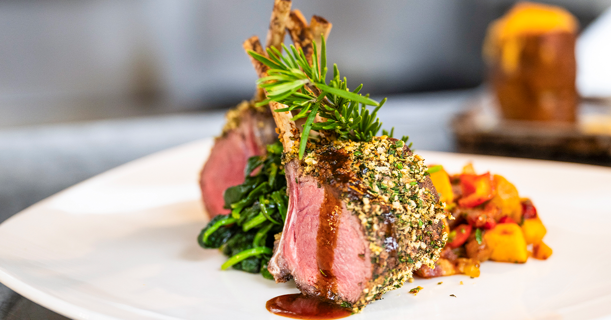 Herb-crusted lamb sliced and plated with vegetables.