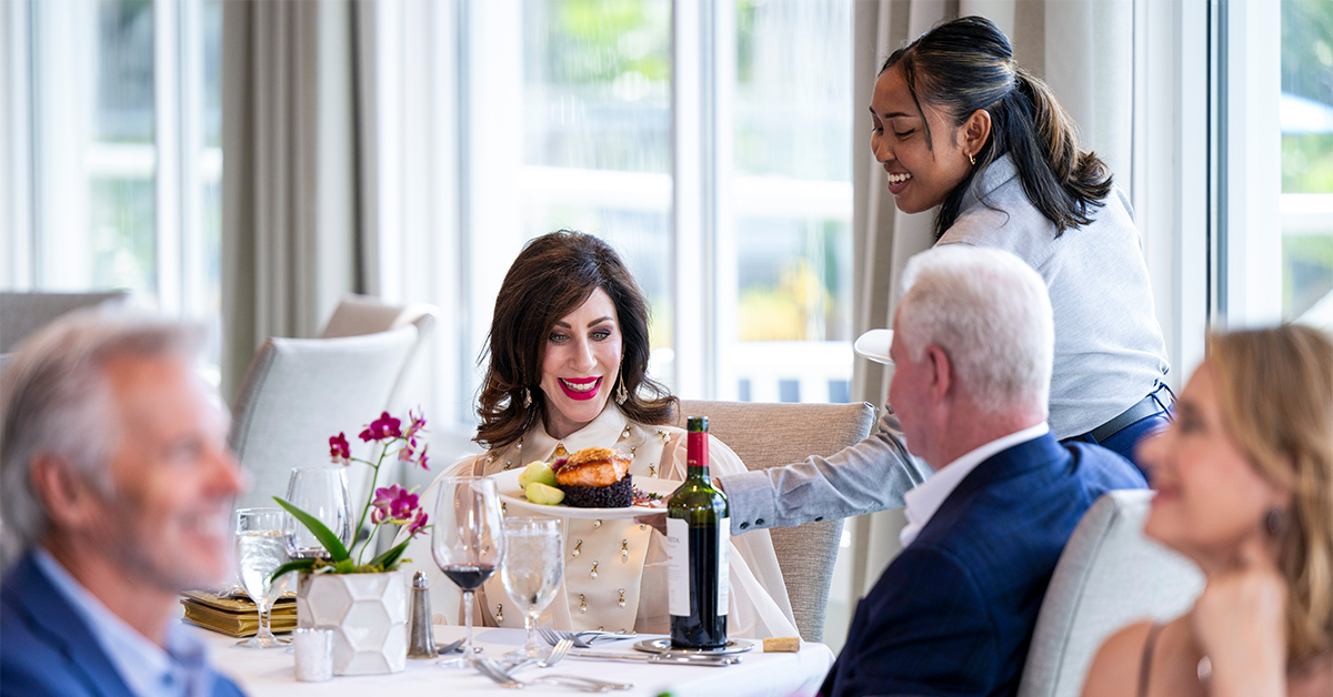 Server presenting a plated meal to guests at a table.