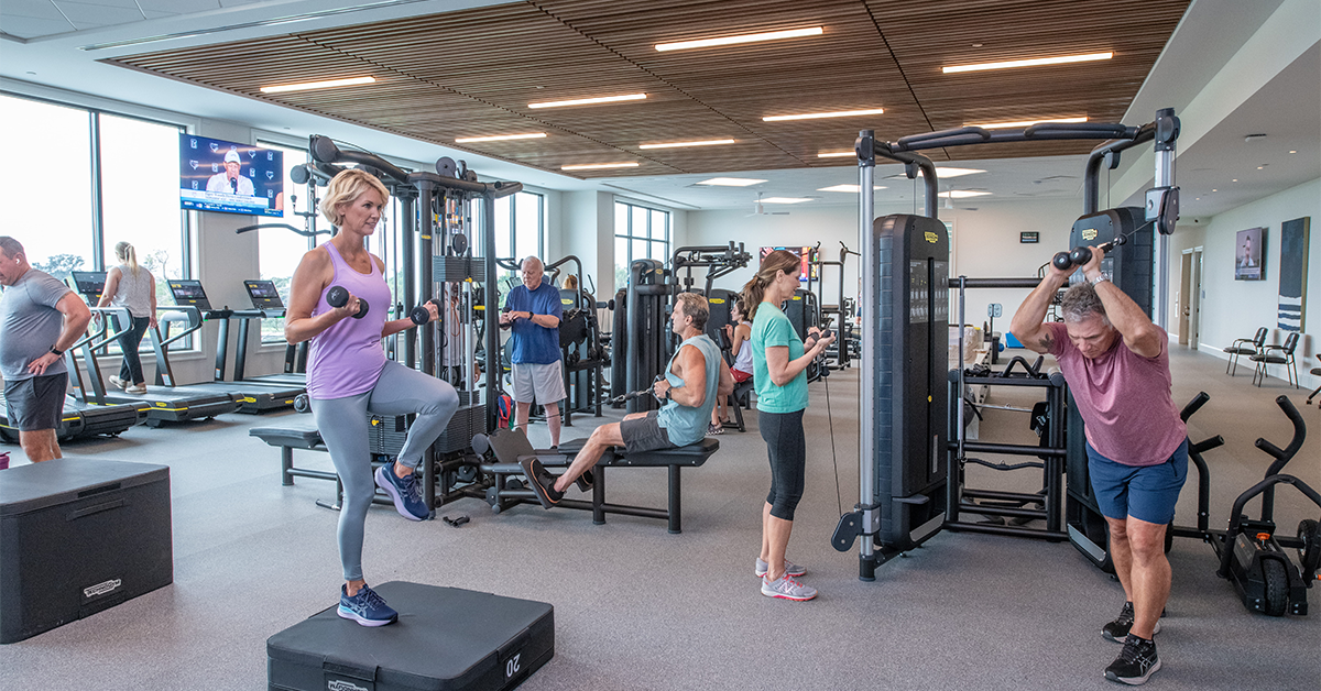 People working out on cardio and weight machines inside modern fitness center.